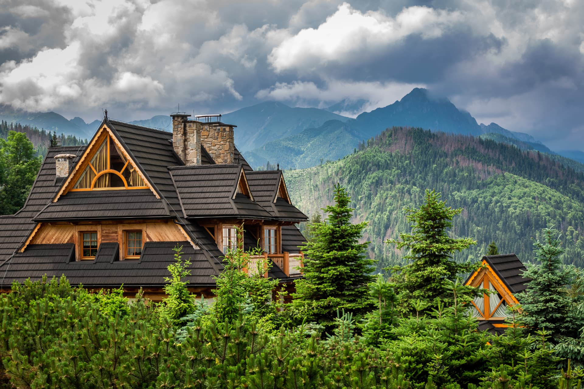 A timber chalet surrounded by trees with dramatic mountains beyond