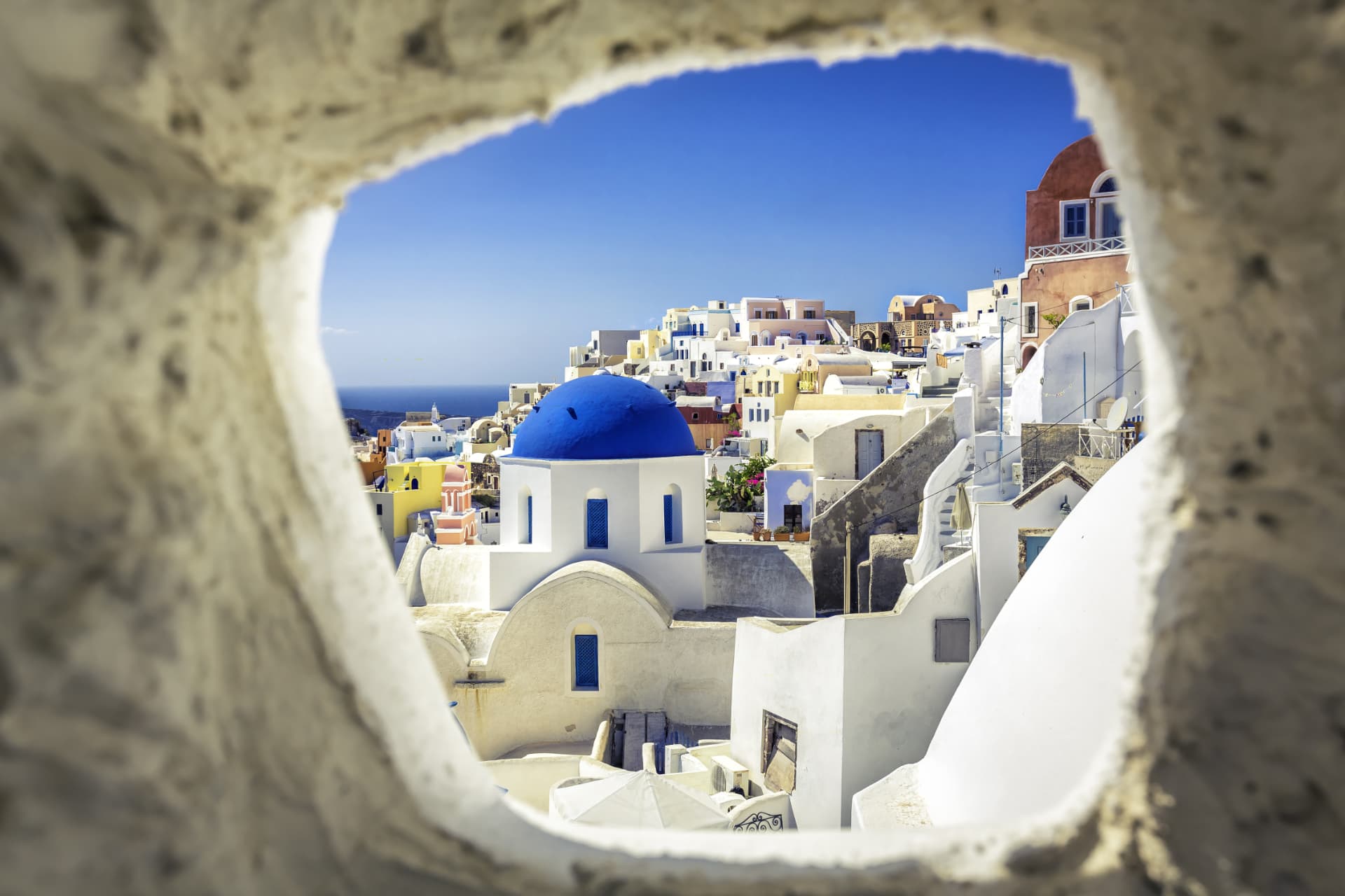 A blue-domed Santorini church framed by a stone opening